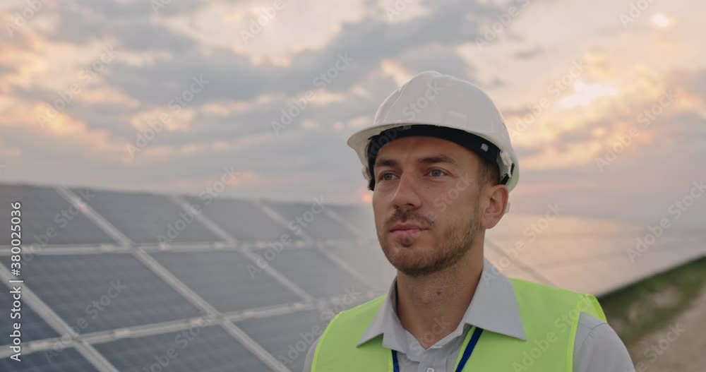 Crop view of caucasian male engineer in uniform. Bearded man in protective helmet walking at solar power plant for examination. Concept of solar station development and green energy. Crop view of caucasian male engineer in uniform. Bearded man in protective helmet walking at solar power plant for examination. Concept of solar station development and green energy.