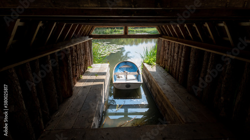 Quadro em tela A small white and blue rowing boat docked up inside a small wooden shack at the
