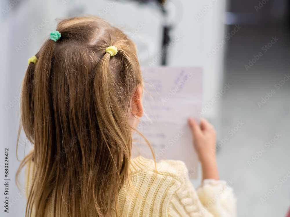 Fototapeta premium Little girls with blond hair are reading a note on a sheet. Back view. Girl in yellow sweater
