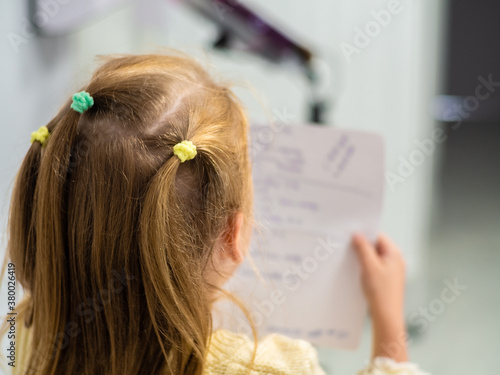 Little girls with blond hair are reading a note on a sheet. Back view. Girl in a yellow sweater