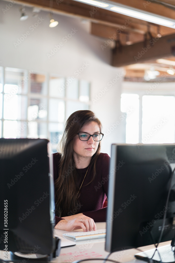 Casual young caucasian woman sits at computer looking at monitor Casual young caucasian woman sits at computer looking at monitor