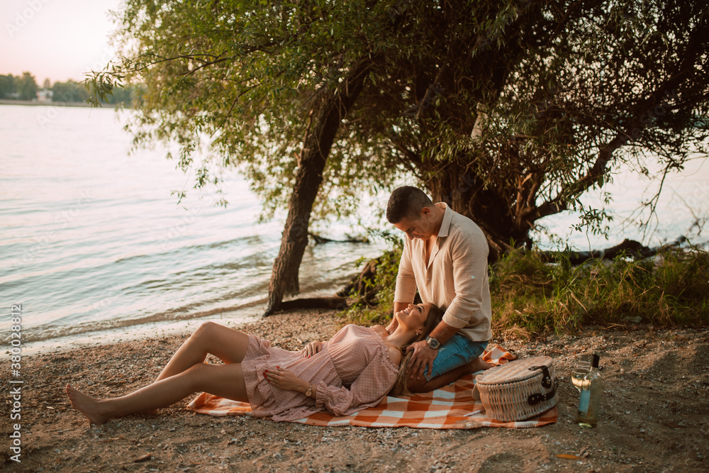 An attractive blonde caucasian woman lies in the arms of a man on the beach. A loving couple on a picnic by the river