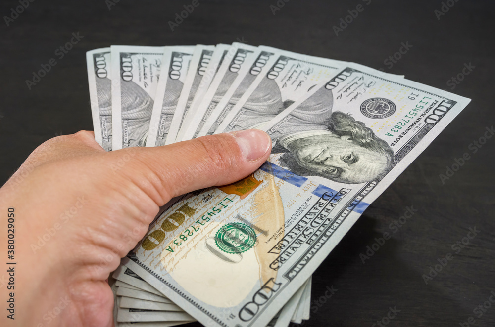 close-up of one hundred dollar bills in a female hand on a black wooden background. close-up of one hundred dollar bills in a female hand on a black wooden background.