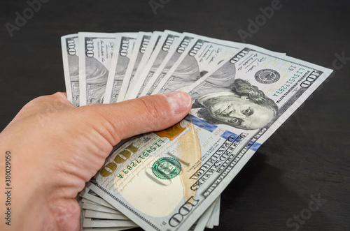 close-up of one hundred dollar bills in a female hand on a black wooden background.