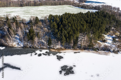 Aerial drone view flying forwards over a frozen lake with trees on the shores