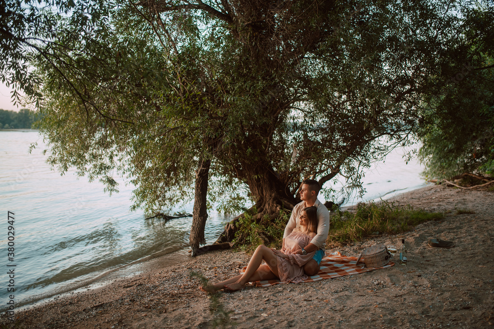 An attractive blonde caucasian woman lies in the arms of a man on the beach. A loving couple on a picnic by the river An attractive blonde caucasian woman lies in the arms of a man on the beach. A loving couple on a picnic by the river