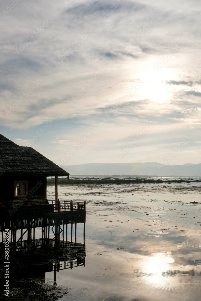 Sunset on Inle Lake with silhouette of traditional floating home Sunset on Inle Lake with silhouette of traditional floating home