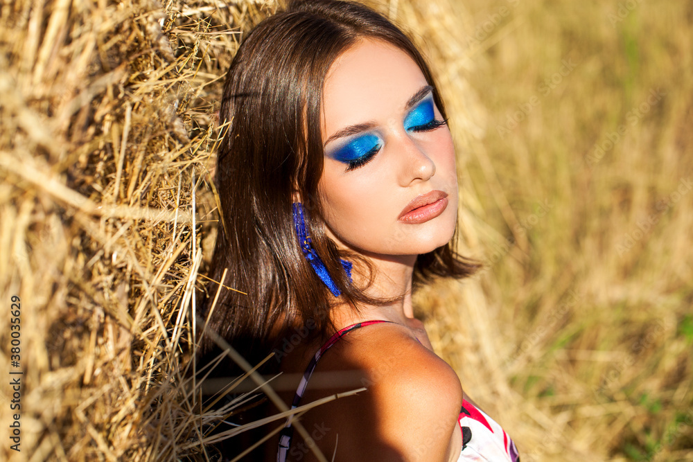 Portrait of a young woman with bright makeup posing on a mown wheat field
