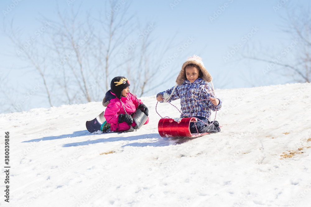 Two sisters happily racing down a snowy hill on sleds Two sisters happily racing down a snowy hill on sleds
