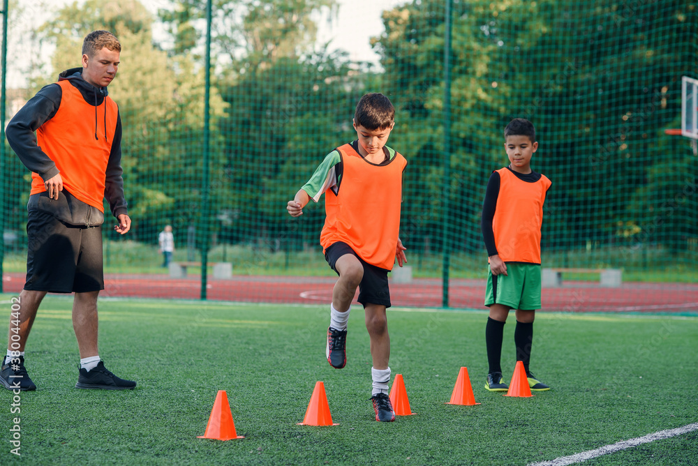 Concentrated junior soccer player running among orange cones that standing on artificial turf at stadium during workout