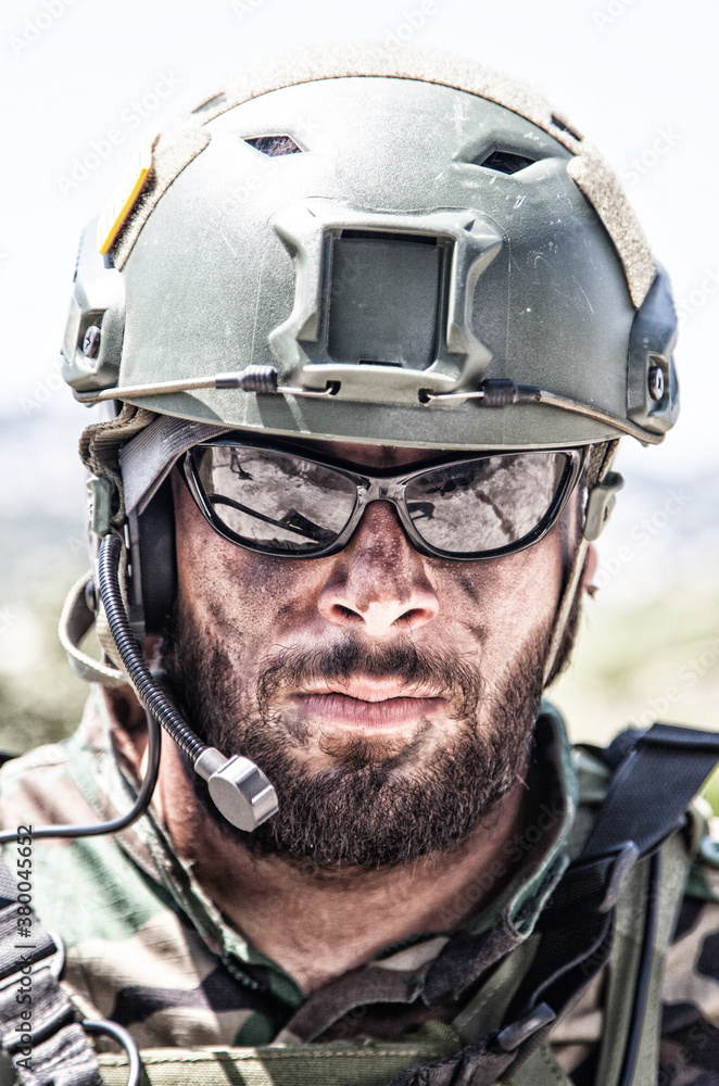 Shoulder portrait of army soldier, special forces fighter, modern warfare combatant with dirty, unshaven face, wearing sunglasses, combat helmet and talking in tactical radio headset during mission Shoulder portrait of army soldier, special forces fighter, modern warfare combatant with dirty, unshaven face, wearing sunglasses, combat helmet and talking in tactical radio headset during mission