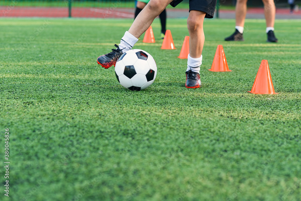 Persistent teen boy in sportswear trains football on soccer field and learns to circle the ball between training cones.