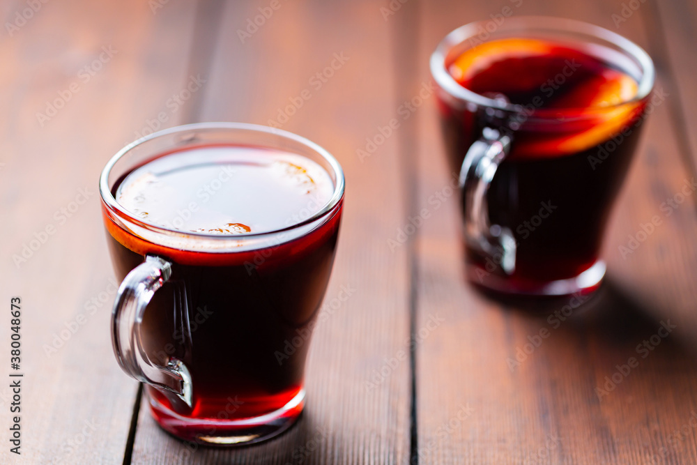 Mulled wine on wooden background. Winter drink traditional for the Christmas holidays. Two glasses of Christmas mulled wine with oranges Mulled wine on wooden background. Winter drink traditional for the Christmas holidays. Two glasses of Christmas mulled wine with oranges