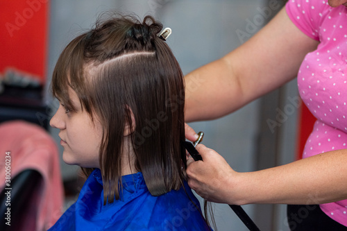 Professional female hairdresser cutting girl's hair in salon