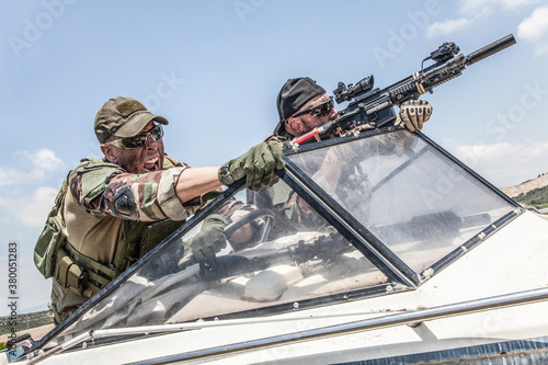 Anti terrorist squad fighters, SEALs team soldiers armed service rifle with optical sigh and silencer, rushing on speed boat, screaming commands to comrades, chasing and attacking enemy on water
