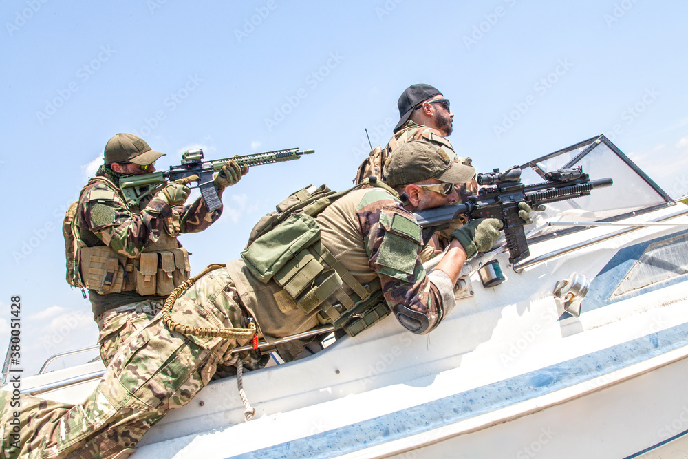 Fototapeta premium Anti terrorist squad fighters, SEALs team soldiers armed service rifle with optical sigh and silencer, rushing on speed boat, screaming commands to comrades, chasing and attacking enemy on water
