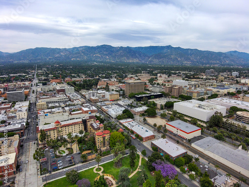an aerial view of the city of Pasadena California with blue sky and interesting cloud covers with buildings and purple trees in the cityscape and mountain ranges USA photo