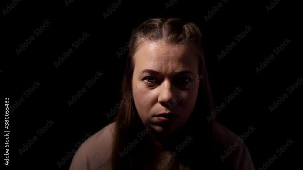 Woman is standing in the studio with black background and speaks aloud. Portrait of caucasian lady with blue eyes talking to someone in darkness. Theme of psychological treatment and psychotherapy. Woman is standing in the studio with black background and speaks aloud. Portrait of caucasian lady with blue eyes talking to someone in darkness. Theme of psychological treatment and psychotherapy.