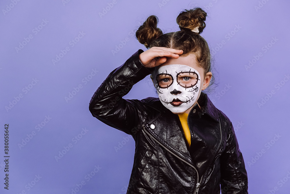 Preschooler girl with serious expression, focused into distance, keeps hand on forehead, wears creative makeup, isolated over purple wall, dressed in Halloween costume. Mexico city's Day of Dead Preschooler girl with serious expression, focused into distance, keeps hand on forehead, wears creative makeup, isolated over purple wall, dressed in Halloween costume. Mexico city's Day of Dead