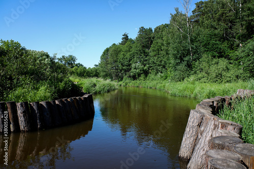 Landscape of a rivier with banks embanked with wooden logs. Sunny summer view.