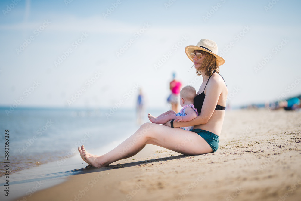 a white woman playing with a baby girl on a beach, sunny weather