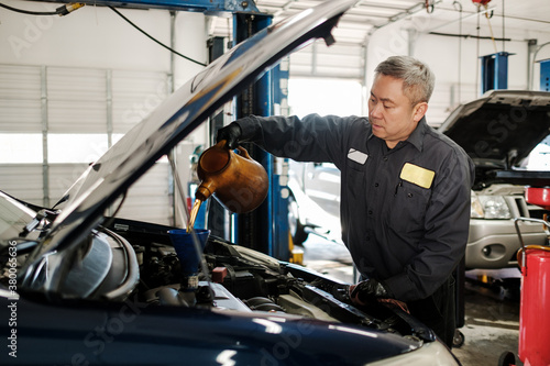 Asian car mechanic performing an oil change in his auto repair s photo