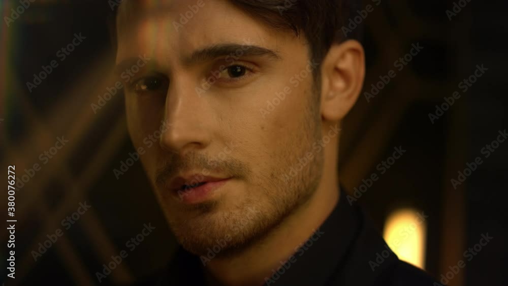 Doubt guy standing indoors. Attractive man gazing at camera in dark interior. Doubt guy standing indoors. Attractive man gazing at camera in dark interior.