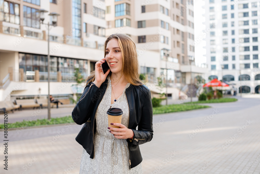 Beautiful woman is speaking on the phone with a cup of coffee at the city street background. Beautiful woman is speaking on the phone with a cup of coffee at the city street background.
