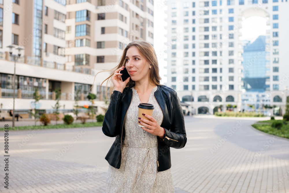 Beautiful woman is speaking on the phone with a cup of coffee at the city street background. Beautiful woman is speaking on the phone with a cup of coffee at the city street background.