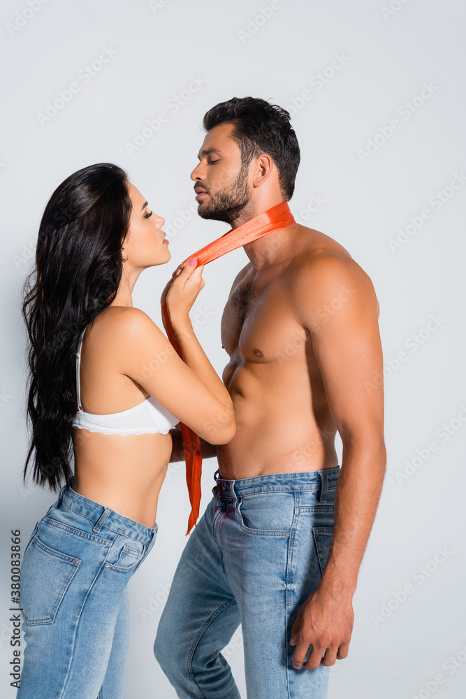profile of seductive woman in bra holding ribbon around neck of muscular and submissive man on white profile of seductive woman in bra holding ribbon around neck of muscular and submissive man on white
