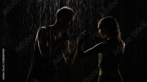 Guy and girl stand in fight stand in the rain. woman and man are ready for fight and stand opposite each other. The girl is dressed in a gray-green top, guy is naked to the waist photo