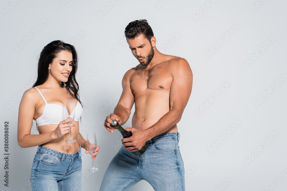 Φωτογραφία muscular man opening bottle of champagne near seductive woman in bra holding gla