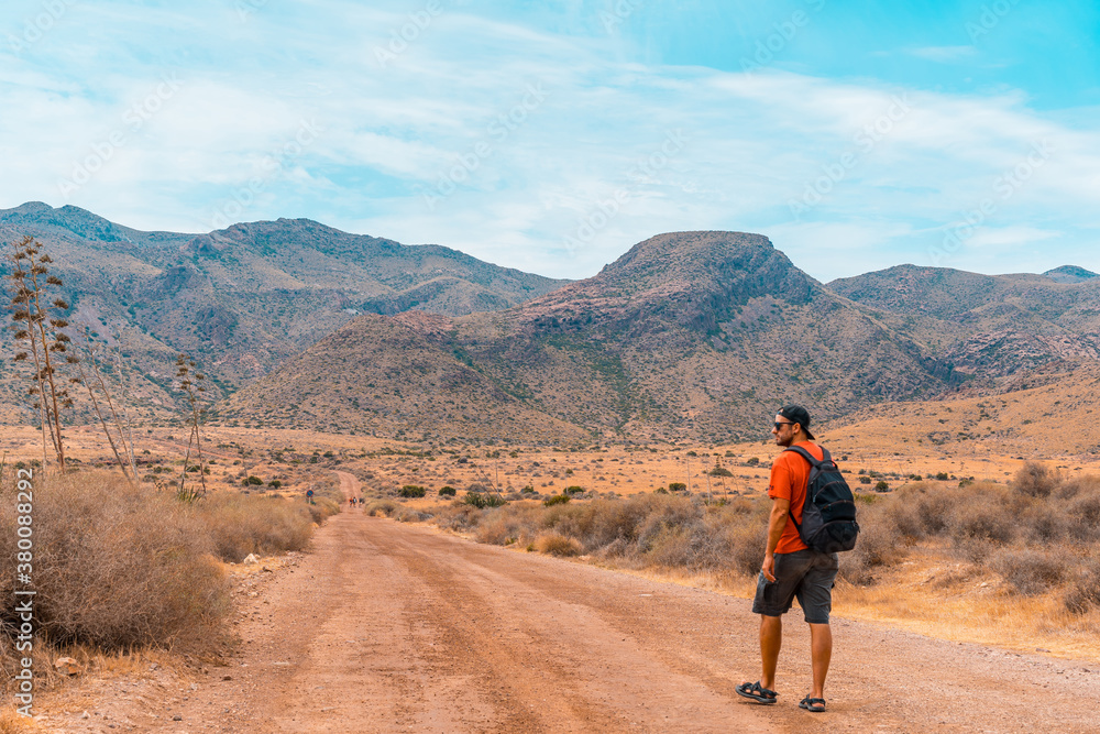 Obraz premium A young man walking along a desert path in the natural park of Cabo de Gata, Nijar, Andalusia. Spain, Mediterranean Sea
