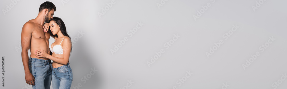 panoramic concept of seductive woman in bra touching muscular man standing on grey panoramic concept of seductive woman in bra touching muscular man standing on grey