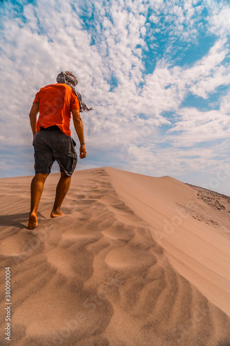 A man with a red shirt and a turban on his head, walking in the desert of the dune of Playa de Mónsul in the natural park of Cabo de Gata, Nijar, Andalucia. Spain, Mediterranean Sea