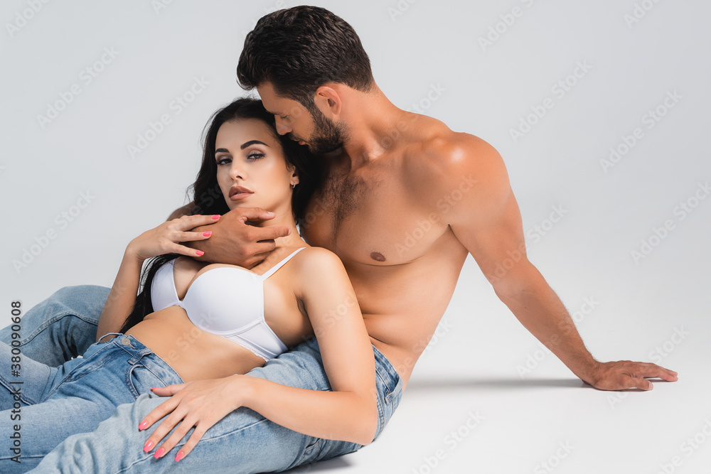 muscular man in denim jeans hugging woman in bra lying on grey muscular man in denim jeans hugging woman in bra lying on grey