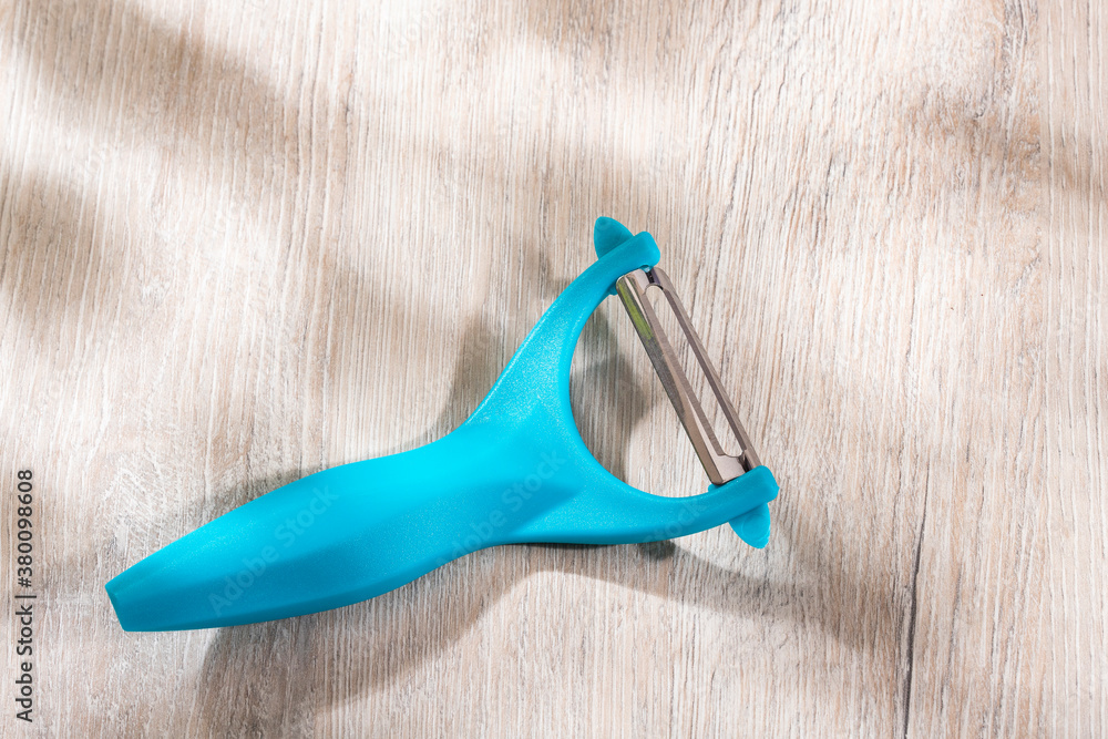 Kitchen potato peeler against wooden background