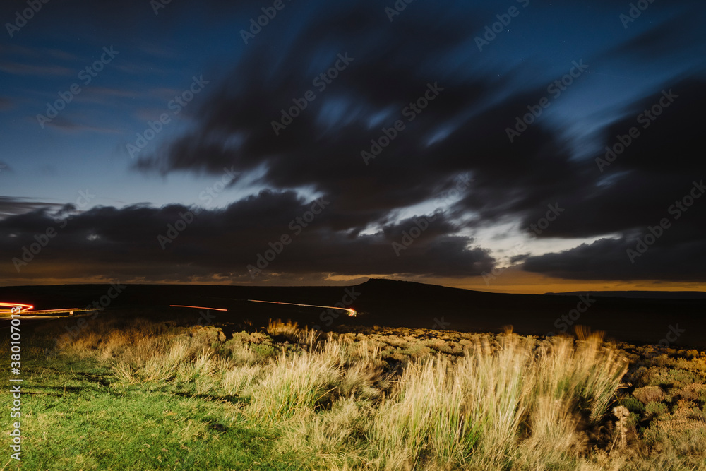 Car light trails below Stanage Edge at night. Derbyshire, UK. Car light trails below Stanage Edge at night. Derbyshire, UK.