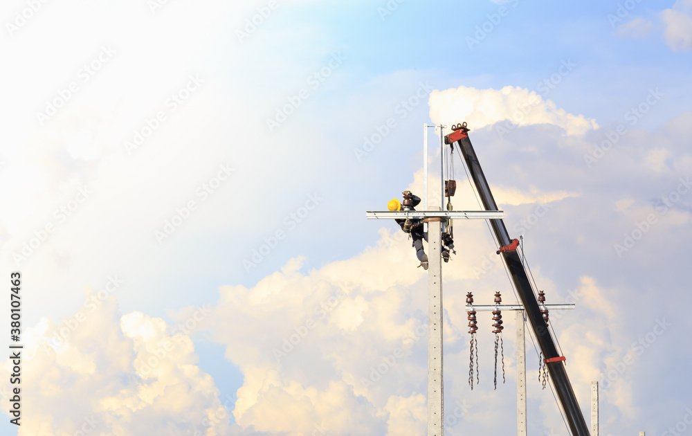 Fototapeta premium A male worker wearing safety equipment (yellow helmets, safety shoes, and seat belt) is working on installing equipment for power lines on high-voltage towers. Using a crane to transport equipment.