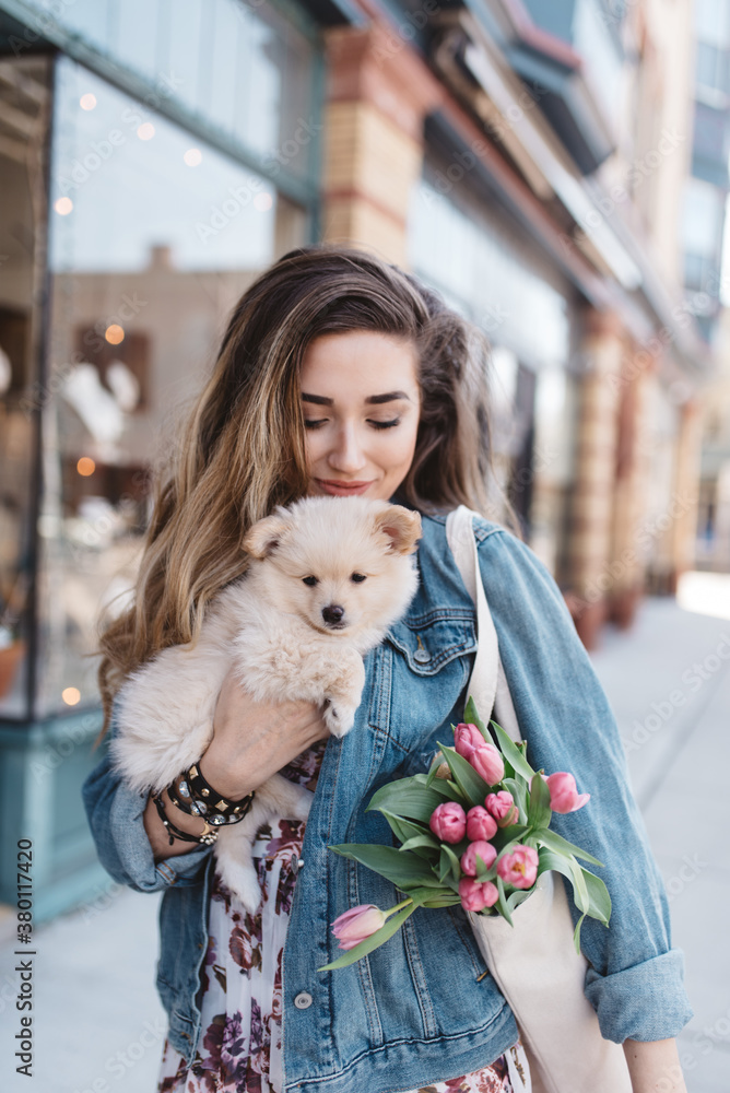 A beautiful young woman walking down a city street shopping with her dog A beautiful young woman walking down a city street shopping with her dog