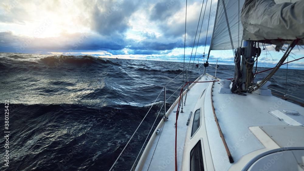 Yacht sailing in an open sea on a winter day. Close-up view from the deck to the bow, mast and sails. Dramatic stormy sky, dark clouds. Epic seascape. North sea, Norway - obrazy, fototapety, plakaty 