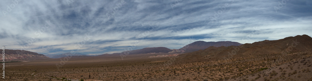 Desolated landscape. Panorama view of the arid desert, sand dune, vegetation and mountains in the horizon under a beautiful blue sky with clouds. Desolated landscape. Panorama view of the arid desert, sand dune, vegetation and mountains in the horizon under a beautiful blue sky with clouds.