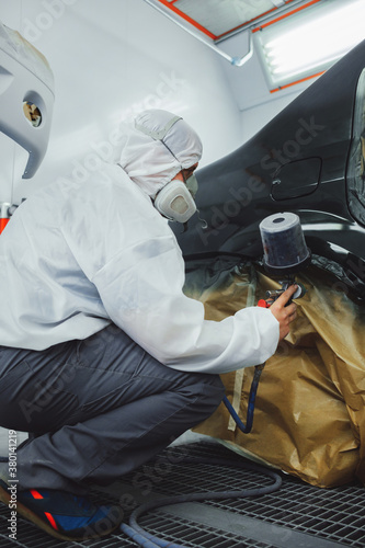 Worker/painter working on car bodywork in paint chamber/workshop.