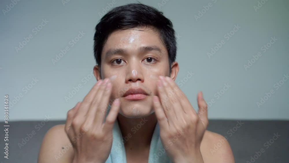 close up young asian man applying sunscreen uv-protection on face and smile while thinking and looking on grey background for advertising product concept close up young asian man applying sunscreen uv-protection on face and smile while thinking and looking on grey background for advertising product concept