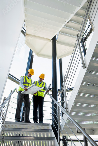 Two Surveyors looking at plans in office building stairway. photo