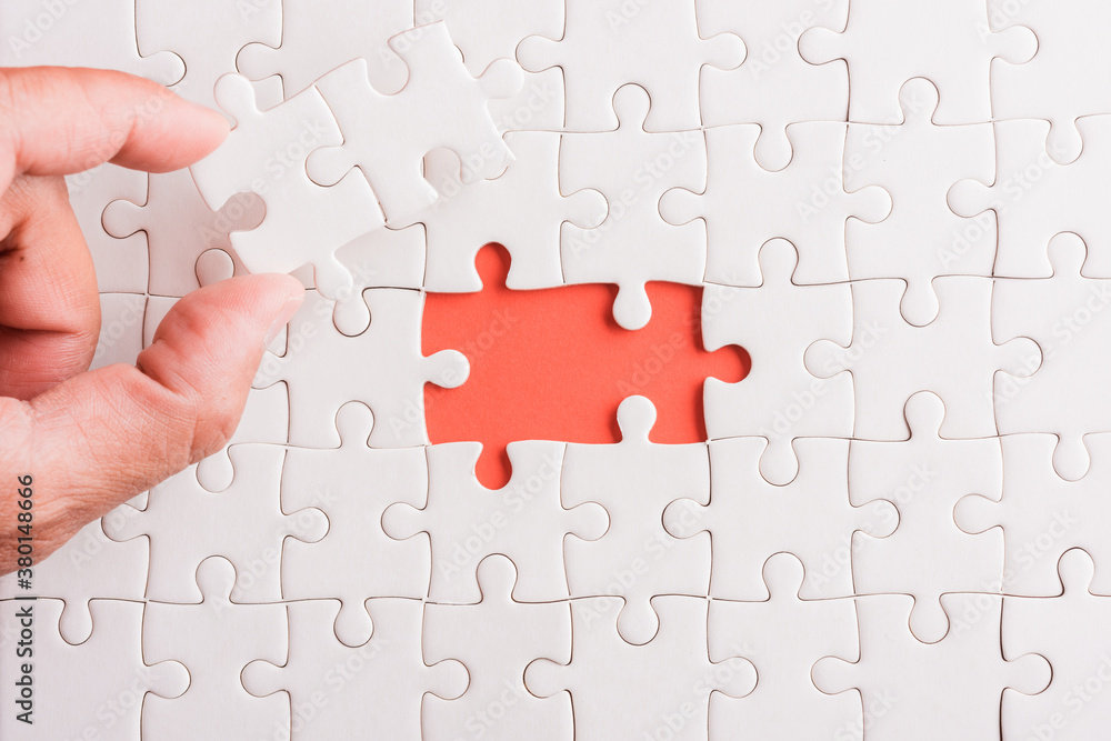 Top view flat lay of hand-holding last piece white paper jigsaw puzzle game last pieces put to place for solve problem complete mission, studio shot on a pink background, quiz calculation concept Top view flat lay of hand-holding last piece white paper jigsaw puzzle game last pieces put to place for solve problem complete mission, studio shot on a pink background, quiz calculation concept