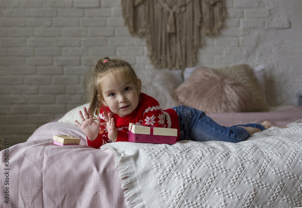 Little girl in a red red christmas sweater plays on the bed with gifts Little girl in a red red christmas sweater plays on the bed with gifts