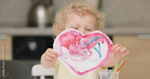 Close up of a a red heart, cutted and drawed by the little girl with watercolors. Presenting it to camera, she is covering her face. photo