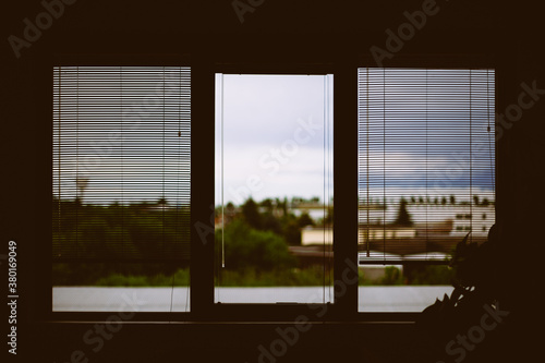 Window with venetian binds against stormy urban landscape photo