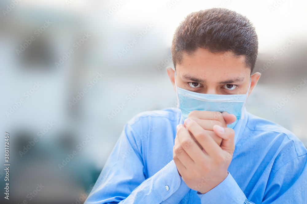 Plakat Portrait shot of a coughing man struggling wearing a medical protective mask posing wearing a blue colored corporate shirt over blurred background.